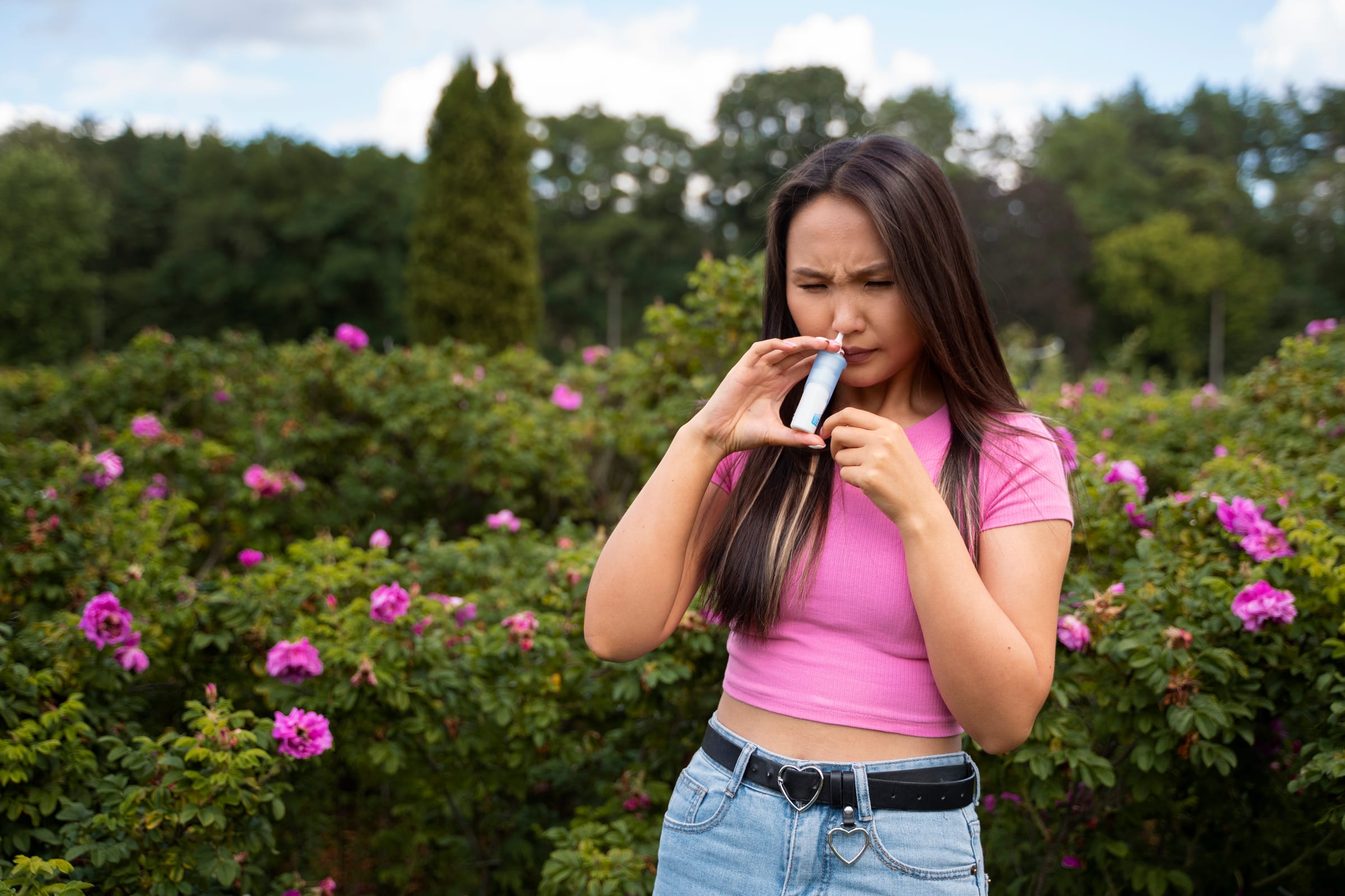 Woman using a nasal spray outdoors among flowering bushes